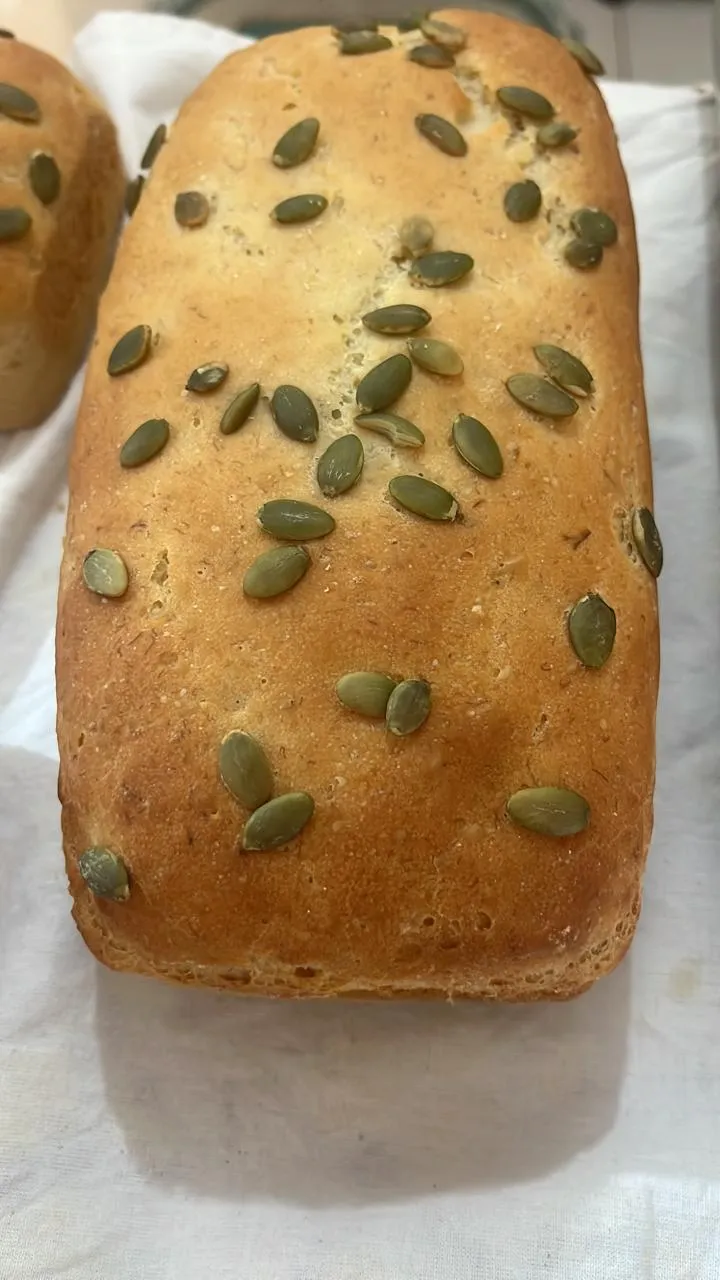 Pão de fôrma dourado com sementes de abóbora por cima, sobre um pano branco